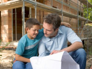 Father and son (6-8) looking at blueprint by house under construction